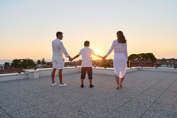 Obraz premium Family On Rooftop Terrace Holding Hands At Sunset With Sea View And Summer Vacation Feeling