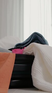 Vertical Screen: A person attempts to pack more clothes into a full suitcase. The task gets harder as the suitcase does not want to close. Clothes are everywhere in the room.