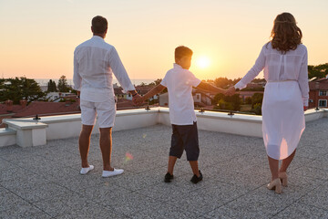 Obraz premium Family Holding Hands on Rooftop Terrace at Sunset With Sea View Over Coastal Town