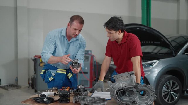 Two mechanics examine engine parts at a repair shop. One gestures while speaking to his colleague. They work beside a lifted car, tools scattered nearby. Teamwork and technical focus