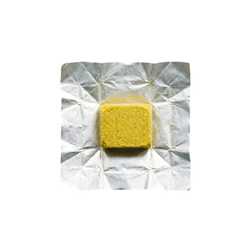 A single yellow bouillon cube unwrapped from its shiny silver foil packaging isolated on transparent background