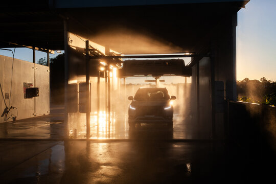Personal vehicle in car wash surrounded my mist spray of water backlit by sunset light