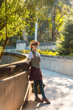 Young woman resting on a concrete ledge in a park with bamboo trees and sunlight. Vertical