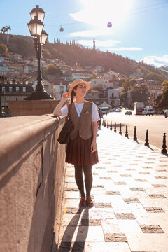 Young woman standing on a sunny bridge with a hillside city background. Vertical