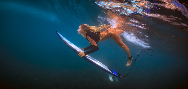 Underwater View of Blonde Female Surfer Paddling on Surfboard in Deep Blue Ocean