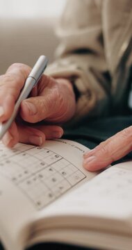 Senior, hands and writing with sudoku in home for number game, pattern or puzzle book. Elderly, male person or empty blocks with cognitive activity for problem solving, thinking or memory in house