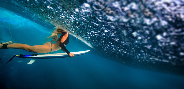 Dynamic Underwater View Of Female Surfer Paddling Beneath Cresting Wave