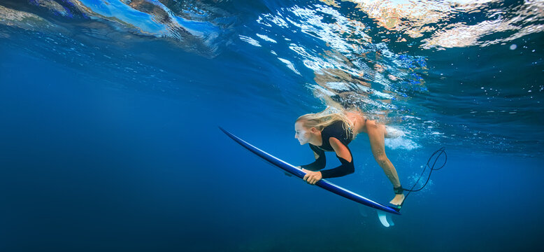 Low Angle Underwater View Of Female Surfer Paddling Toward Sunlit Surface
