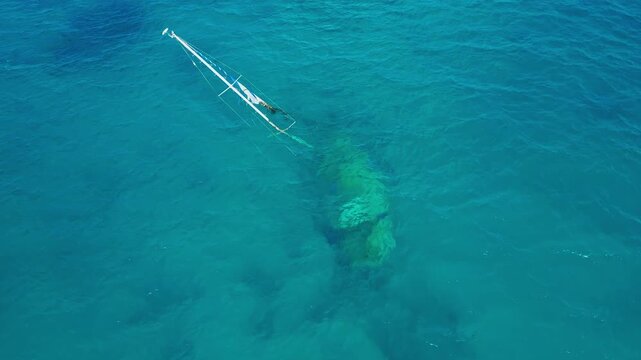 Aerial shot stranded sailboat near reef, shallow turquoise sea exposing mast and shadowed hull, calm swell with sun glint, drone circumnavigating target for inspection, mapping, Maldives