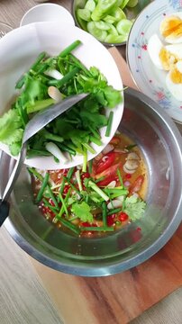 Mixing ingredients like chopped chilies, onions, garlic, and tomatoes into a metal bowl to create a Thai salad spicy dressing. Traditional Thai culinary preparation