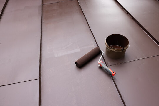 Painting tin metal roof with roller and brown paint. House roofing repair