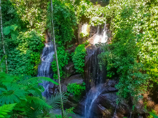 Multiple tropical waterfalls cascading through dense jungle with Balinese temple shrine in background, Bali, Indonesia © dvad