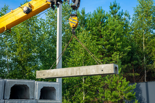 Crane truck unloads precast concrete channel outdoors. Concept: heavy cargo unloading
