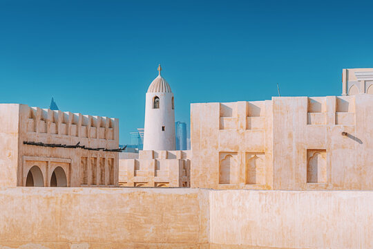 Souq Waqif's historic buildings and mosque tower contrast with Doha's modern city skyline under a clear blue sky