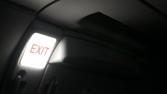 view inside airplane cabin to the emergency exit door with light signal for exit at door while flying take off from airport, light sign board for emergency door in aircraft cabin