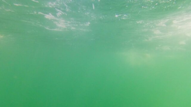 Cinematic underwater shot of a boat hull gliding through murky green sea water with surface light rays. Useful for marine biology, sailing, and ecofriendly ocean travel concepts.
