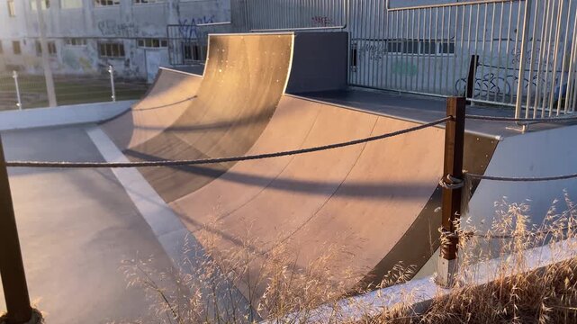 Empty skatepark showing ramps and grind rail under warm, glowing sun, creating a sense of urban leisure and modern design