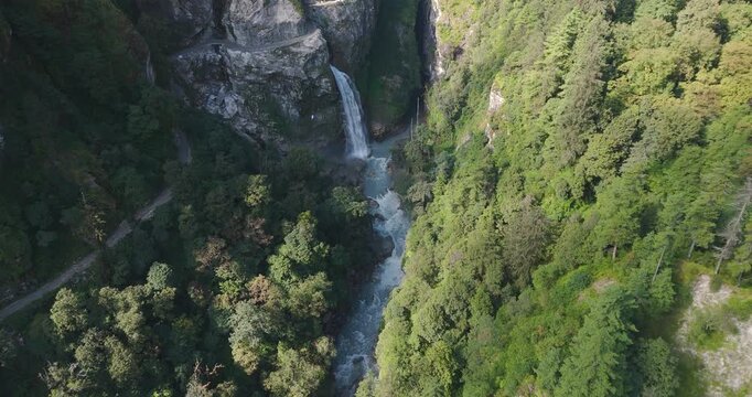 Annapurna Circuit Nepal, aerial view of Danaque waterfall plunging from a rocky cliffside into the winding Marsyangdi River gorge surrounded by forest trees in the Manang region.