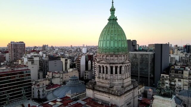 Green copper dome of the Palace of the Argentine National Congress rises over dense Buenos Aires city blocks at sunset, with the neoclassical roofline surrounded by modern towers.