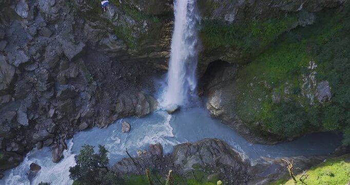 Annapurna Circuit Nepal, aerial push in shot moving closer to Danaque waterfall plunging from a steep rocky cliff into the blue waters of the Marsyangdi River gorge near Manang.
