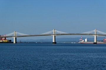 Obraz premium Symmetrical view of a modern cable stayed bridge over the calm blue sea with ships in harbor under a clear sky, Fukushima Japan.