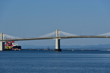 Fototapeta premium Modern concrete infrastructure and large cable stayed bridge over the calm blue sea with cargo ship in port, Fukushima Japan.