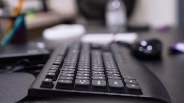shot of a black computer keyboard and mouse on a modern dark office desk. The shallow depth of field blurs the background workspace items, creating a corporate or work from home setting.