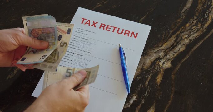 Hands counting cash beside a tax return form and pen, representing finance, paperwork, payment and personal accounting.
