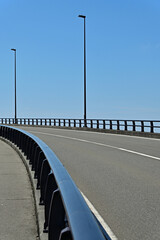 Fototapeta premium Abstract vertical view of an empty curved highway roadway and street lights under a clear blue sky, Fukushima Japan.