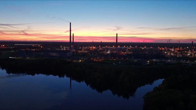 Drone yaws left above Orlen Lietuva refinery glowing beneath colorful sunset sky