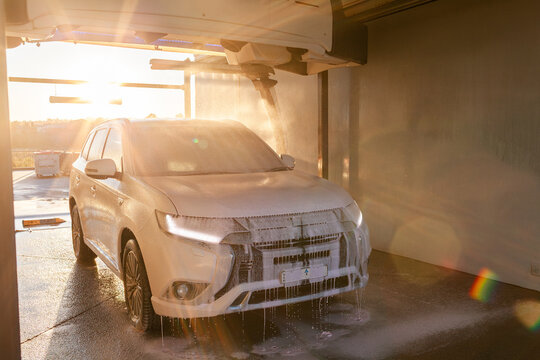 Vehicle covered in soapy suds and spray in automatic car wash bay in golden Australian light
