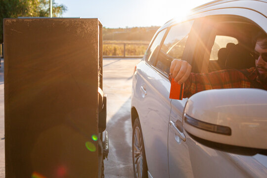 Man leaning from vehicle to tap debit card on car wash payment machine in golden light