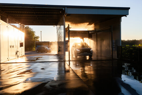 Personal vehicle in car wash surrounded my mist spray of water backlit by sunset light
