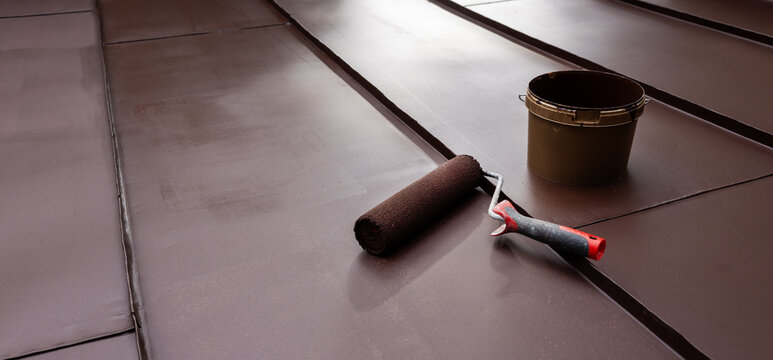 Painting tin metal roof with roller and brown paint. House roofing repair service. copy space