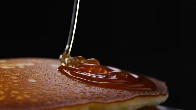 Amber syrup pouring onto golden pancake, creating glossy pooled ring under low key studio lighting, with rich caramel shine, warm tones, and appetizing dessert presentation