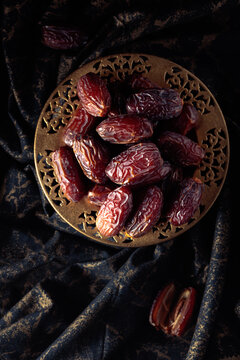 Dates fruits in a golden bowl on black fabric with gold ornamentation.
