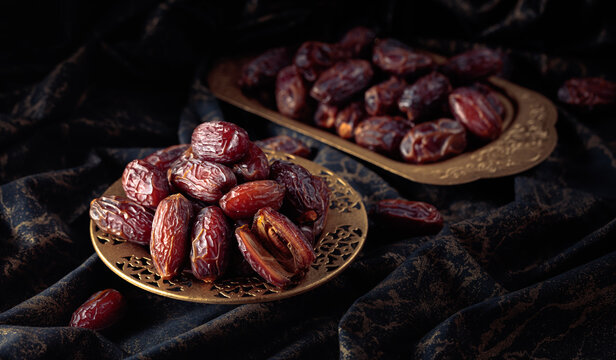 Dates fruits in a golden bowl on black fabric with gold ornamentation.