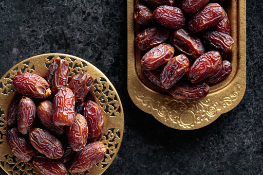 Dates fruits in a golden bowls on black stone table.