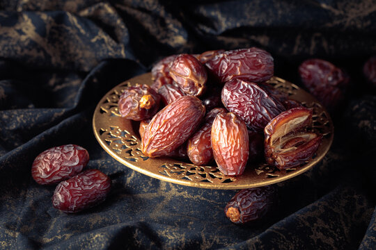Dates fruits in a golden bowl on black fabric with gold ornamentation.