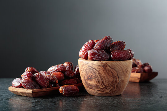 Dates fruit in wooden dish on a black table.