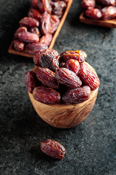 Dried dates fruit in wooden bowl on a black table.