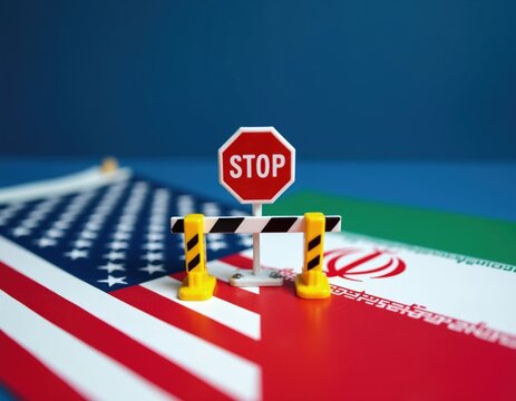 Miniature stop sign, yellow barrier stand on American, Iranian flags. Symbolic road block object represents geopolitical tensions. Toy construction equipment on fabric national banners denotes