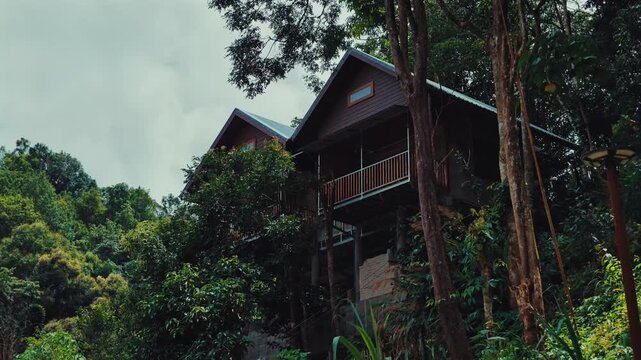 Wooden mountain cabins surrounded by lush tropical jungle on forest hillside, Scenic rainforest lodge retreat with elevated architecture, Mae Kampong Thailand 4k