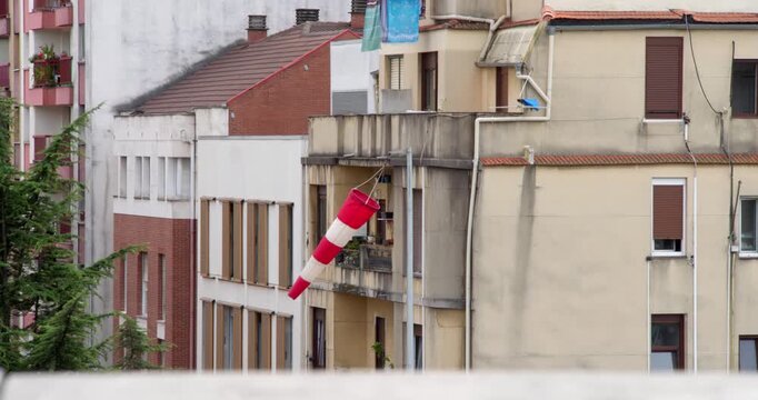 Windsock on Balcony: A red and white striped windsock hangs from a balcony against a backdrop of residential buildings, indicating wind direction.