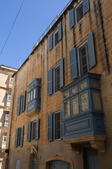 Obraz premium Traditional blue wooden balconies and shutters on historic limestone building facades in Malta.