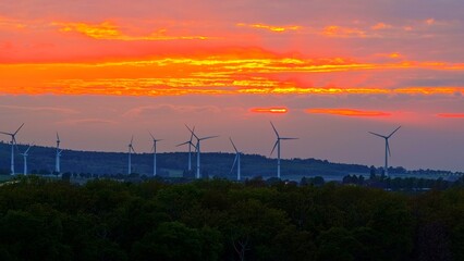 Obraz premium Wind Turbines at Dramatic Golden Sunset Over Green Fields