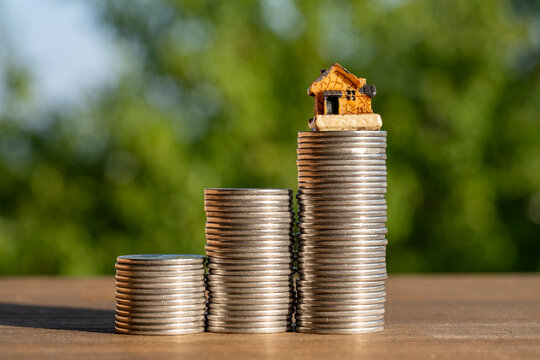 Small house model on top of growing coin stacks with green bokeh background, closeup. Concept for mortgage, savings, property investment, real estate market growth, or financial planning