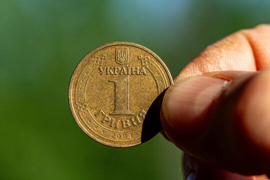 Closeup of hand holding Ukrainian one hryvnia coin from 2004 against blurred green nature background. Symbol of Ukraine national currency, finance, banking, or national economy