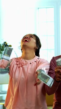 Indian Asian young couple happily counting a stash of Indian five hundred rupee currency notes and joyfully throwing them in the air after winning lottery or bonus standing in living room