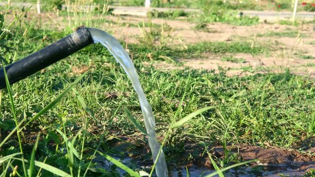 Water pouring from a pipe onto green grass field close up